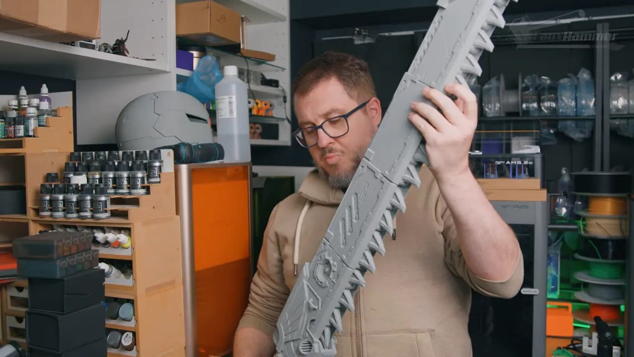 Person holding a large printed cosplay prop in the workshop with Bambu P2S in the background