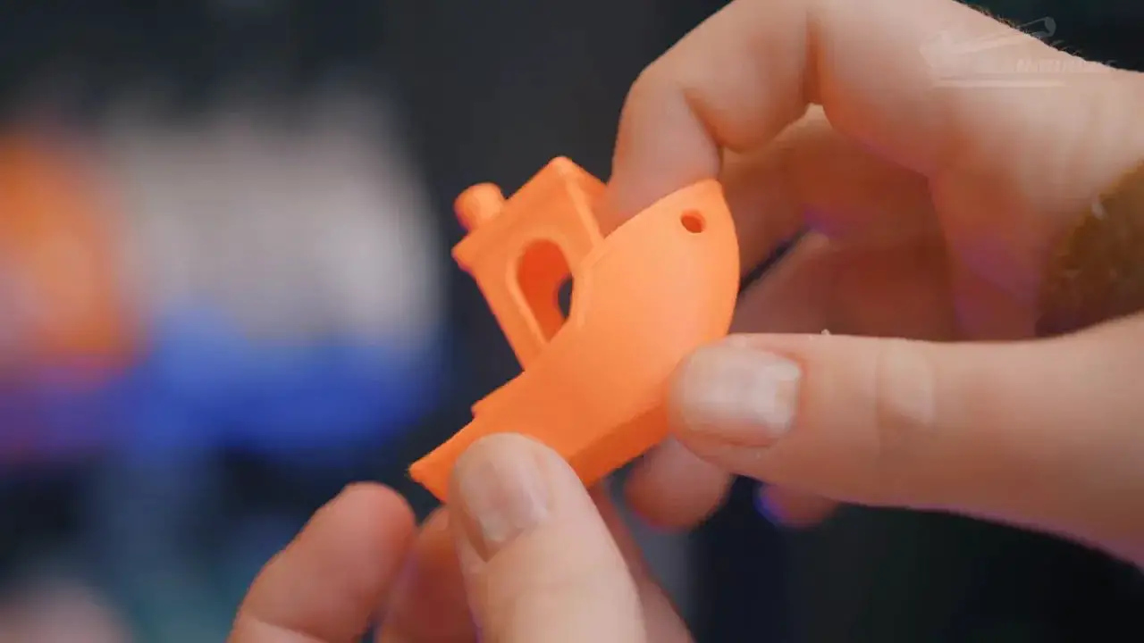 Hand holding an orange 3D-printed part with a complex cutout pattern