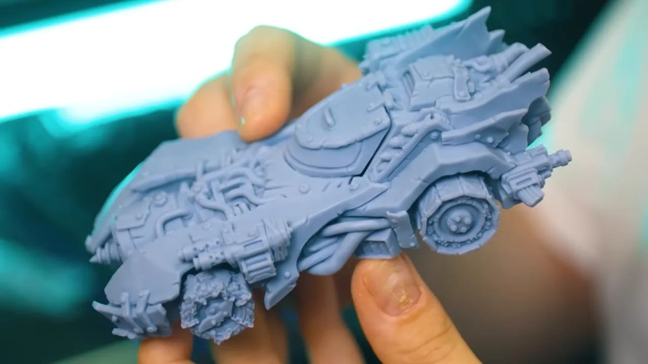 Close-up of a detailed resin vehicle miniature held in fingers showing crisp surface detail from HeyGears Reflex