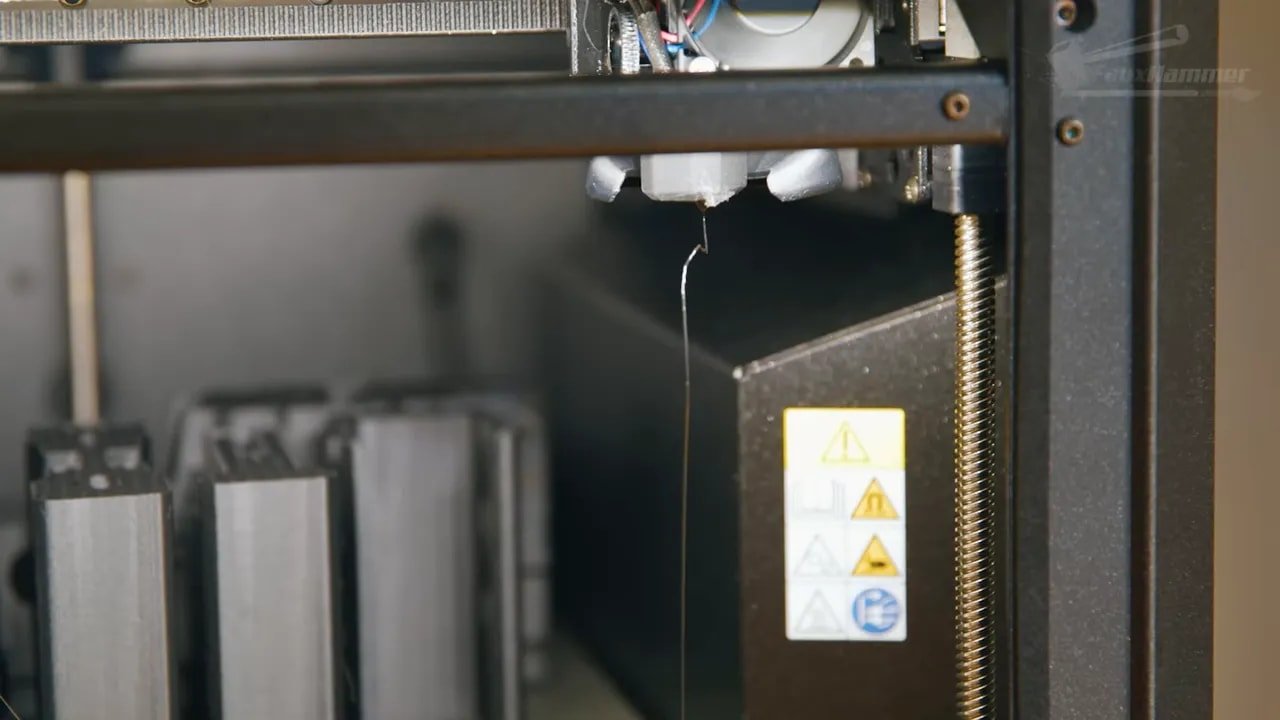 Close-up of Prusa Core One enclosed hotend area with filament line and caution label