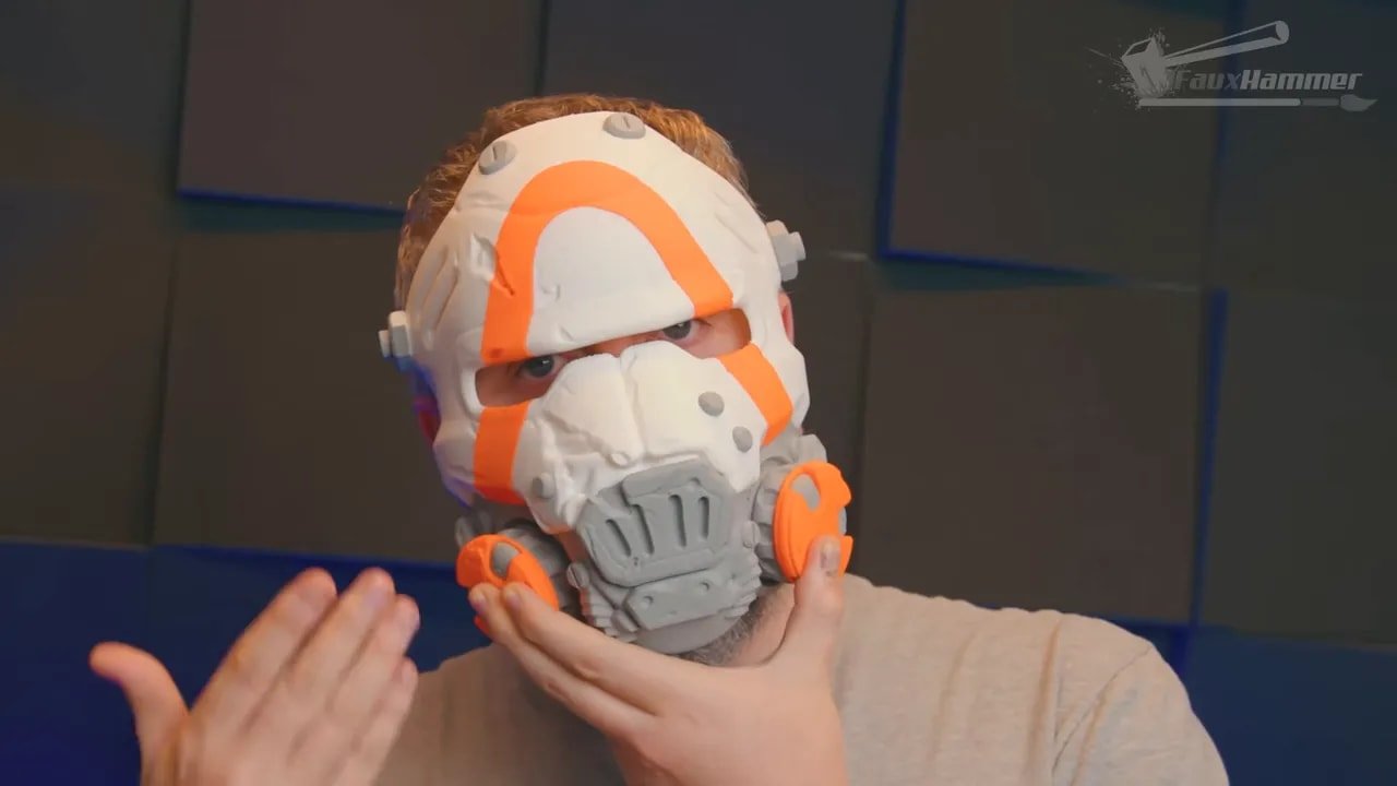 Person holding a printed cosplay mask with orange and white multi-colour details